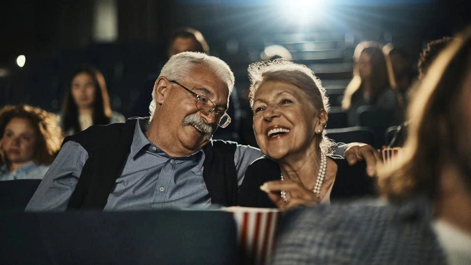 Elderly couple sitting closely in a movie theater with popcorn, enjoying a film together.