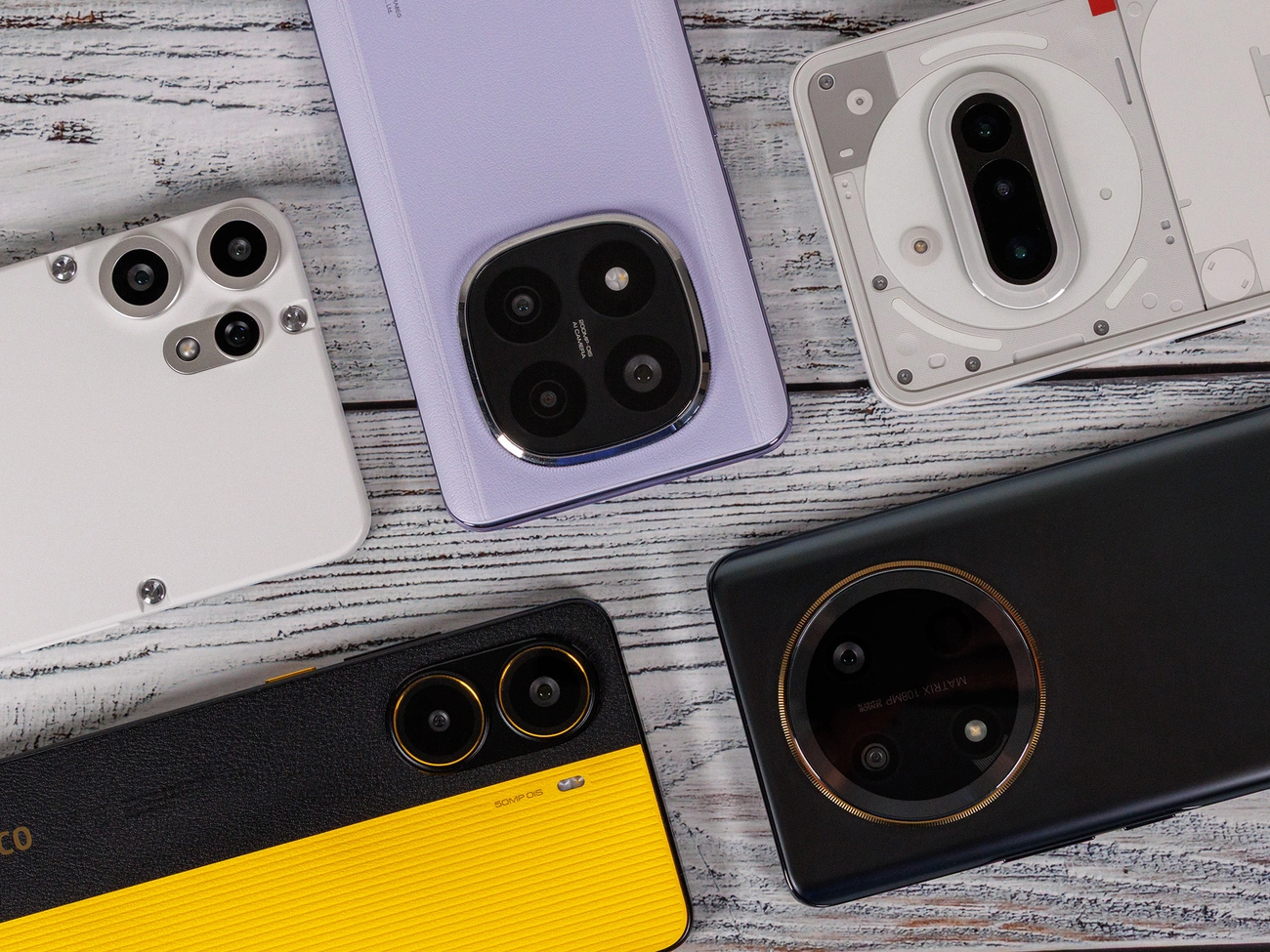 Top view of five smartphones with varied camera designs arranged on a wooden surface, representing budget models under 300 dollars/euros.