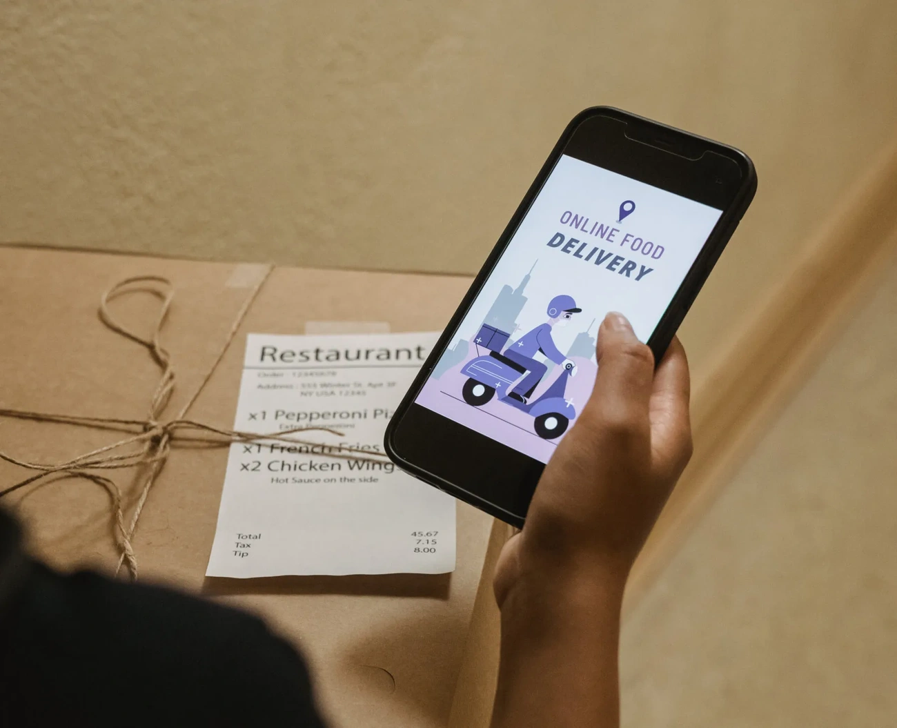 Person holding a phone with an online food delivery app while a tied food box and receipt lay on the table.