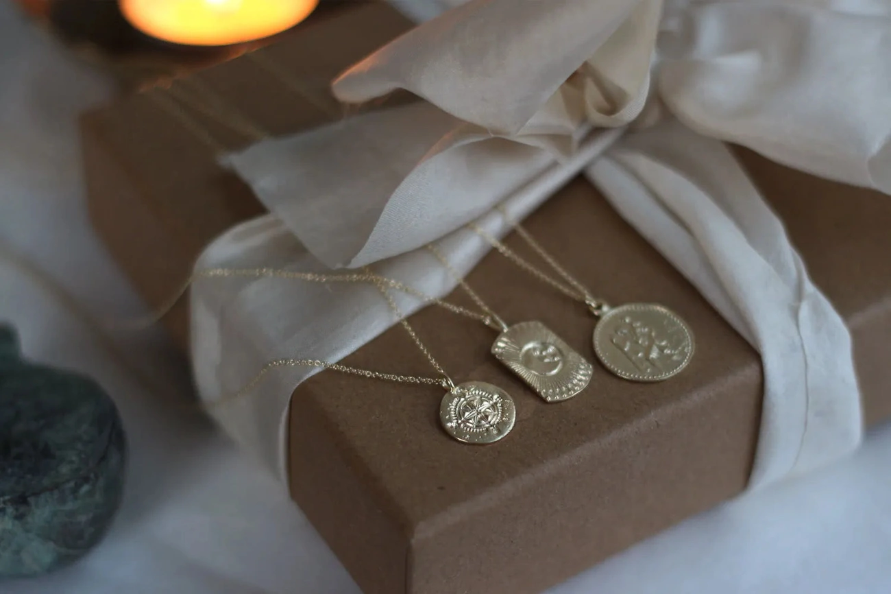 Three gold pendant necklaces displayed on a wrapped gift box with a white fabric bow, evoking a Christmas gift idea.