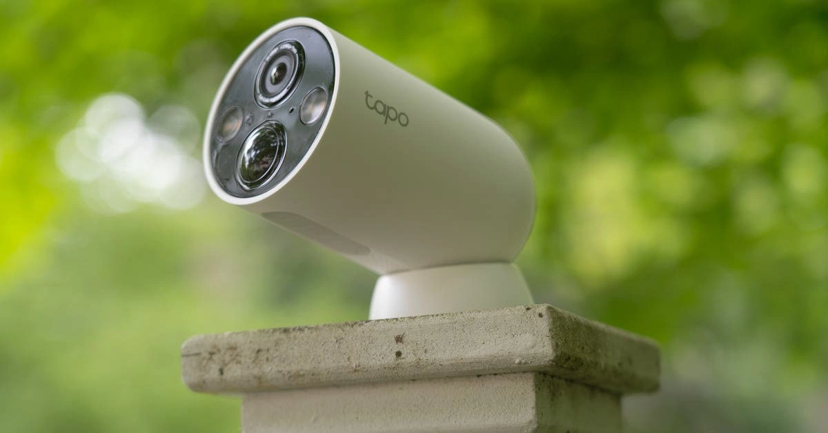 Close-up of a Tapo outdoor security camera mounted on a concrete pillar with a blurred green background.