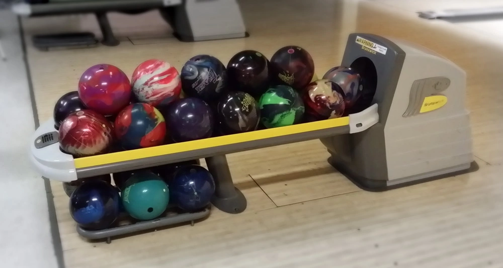 Various colorful bowling balls neatly arranged on a ball return rack at a bowling alley lane.
