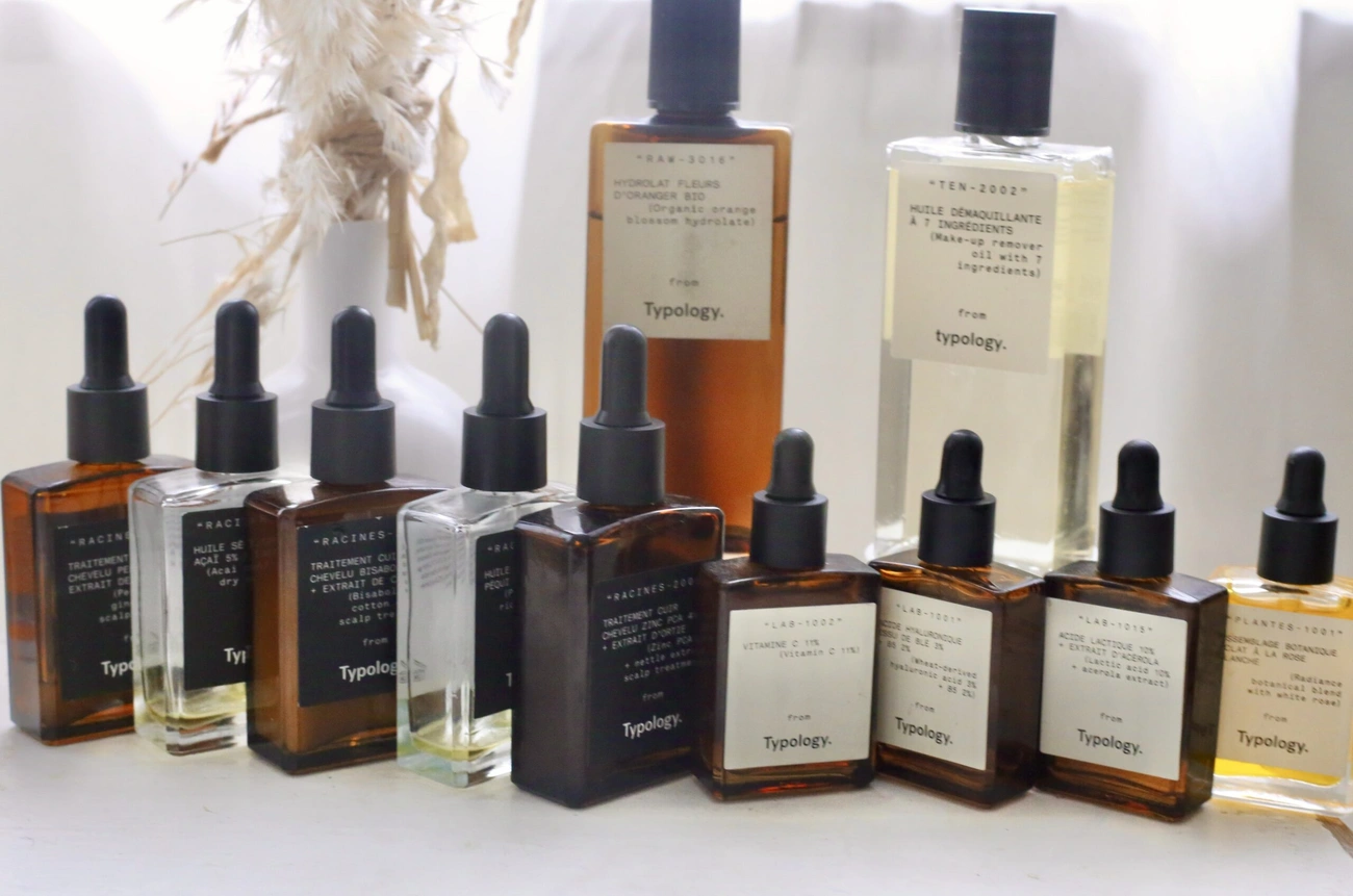 Various Typology skincare products in amber and clear bottles with black droppers and labels, arranged on a white surface.
