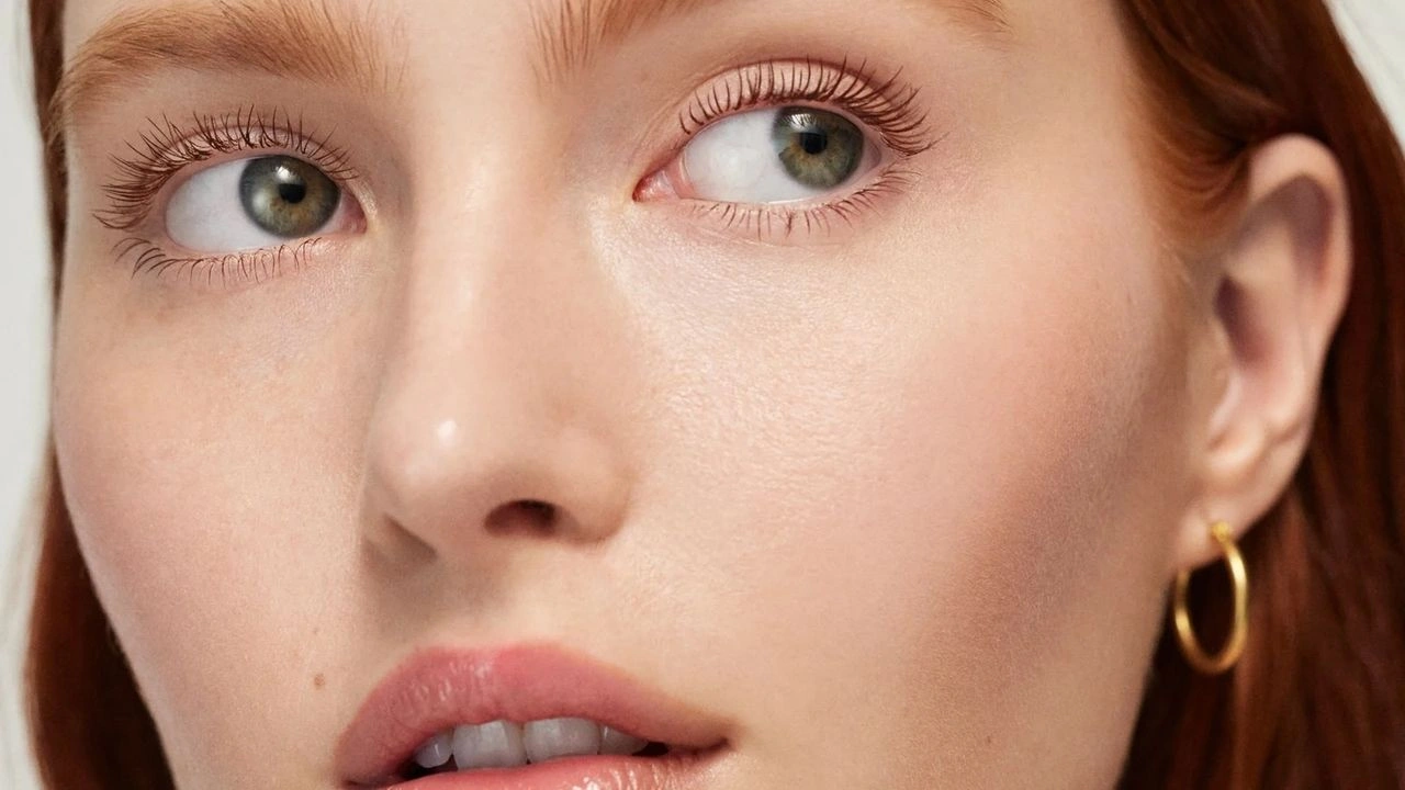 Close-up of a person with red hair wearing a gold hoop earring, showcasing clear skin and natural makeup.