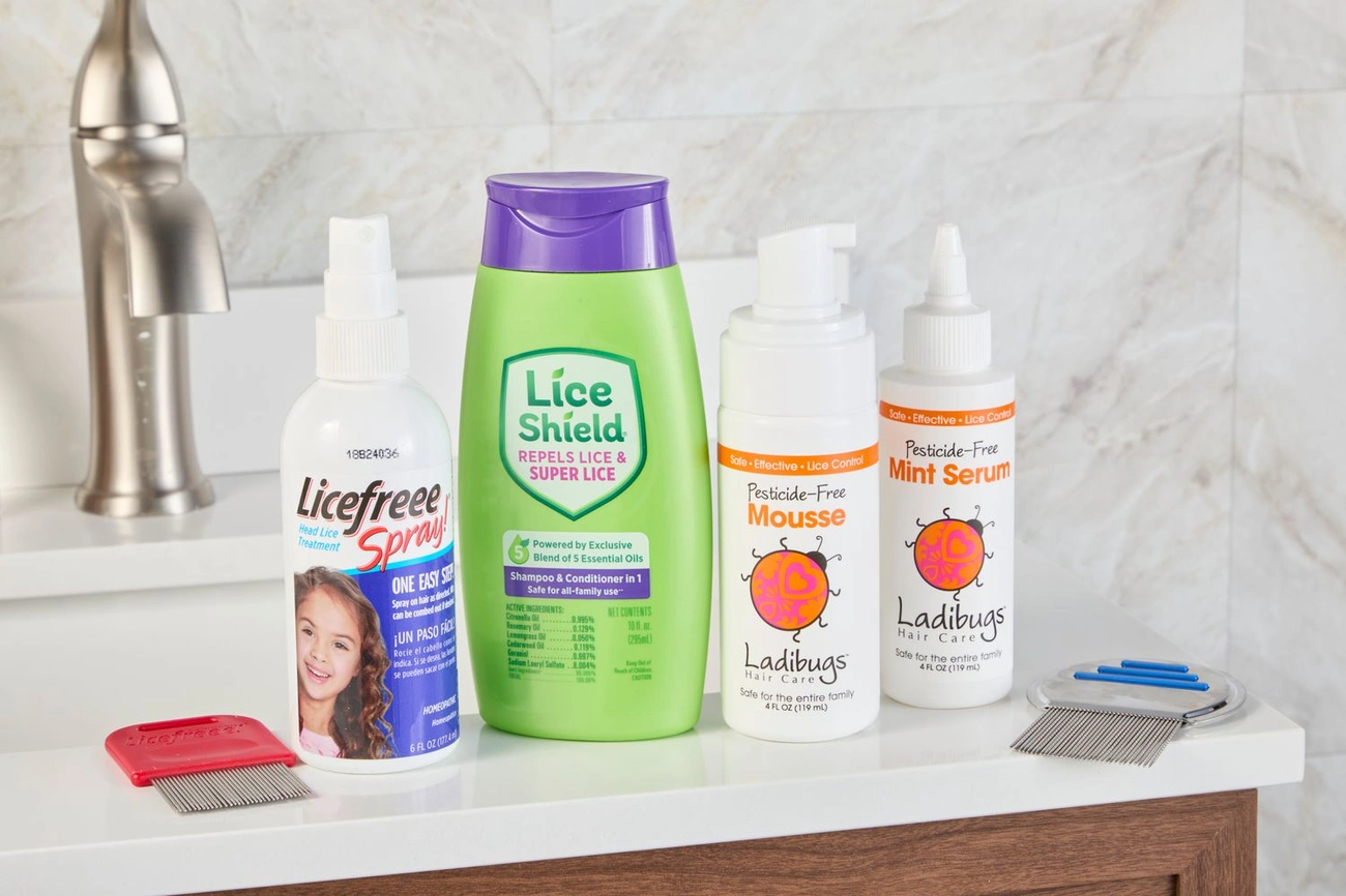 Various lice treatment products and metal lice combs displayed on a bathroom counter near a faucet.